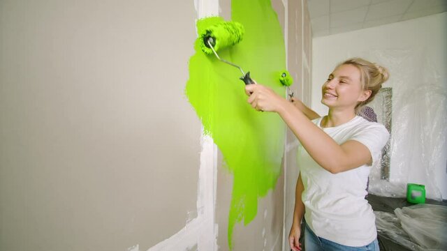 Portrait of a happy young girl painting a drywall wall in green, with her boyfriend. A young family paints over the wall