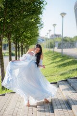 Pregnant woman posing in a blue dress on a background of green trees.