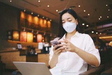 Woman wearing medical mask and smart phone in coffee shop.