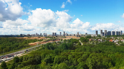 Obraz premium Panorama of the city with parks from a height. Blue sky with clouds on buildings under construction.