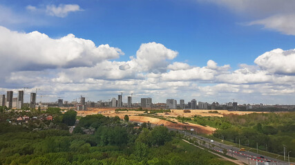 Fototapeta na wymiar Panorama of the city with parks from a height. Blue sky with clouds on buildings under construction.