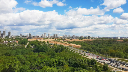Obraz premium Panorama of the city with parks from a height. Blue sky with clouds on buildings under construction.