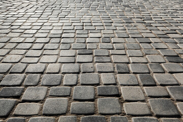 The surface is paved with road tiles of different sizes (multi format). The uneven (melange) color of the tile makes it look like a natural stone. Perspective viewpoint.