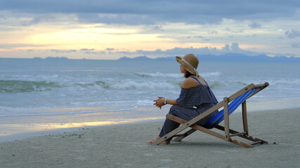 Asia woman sitting on beach chair and enjoying during the sunset on the beach. Summer vacation concept.