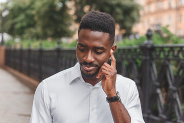 Young stylishly dressed black male, enjoying music with wireless earphones walking outdoors