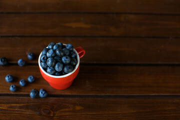 Red cup of bilberries and blueberries on a wooden table . Healthy food for diet. Dark background.