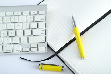 White office desk table with blank notebook, computer keyboard and other office supplies. Top view with copy space, flat lay.