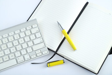 White office desk table with blank notebook, computer keyboard and other office supplies. Top view with copy space, flat lay.