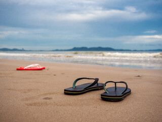 Closeup of colorful sandles on the beach sand with ocean in the background.