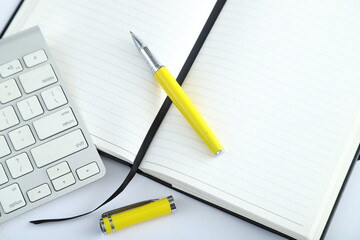 White office desk table with blank notebook, computer keyboard and other office supplies. Top view with copy space, flat lay.