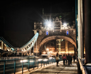 Obraz premium Tower bridge lit up at night time busy with people and traffic crossing.