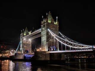 Tower bridge lit up at night from the Thames embankment.