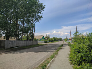 Russian village, a city road passes near a path and houses in Kamen-na-Obi, Altai, Russia. Vertical.