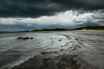 The tide has turned at Low Newton-by-the-Sea but clouds are heavy before the rain on a warm summers day.