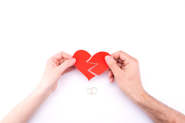 Female and male hands hold a broken heart on a white background with wedding rings. Marriage problems, divorce