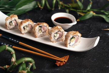 sushi with chopsticks. Sushi lie on white plate. Bamboo branches on black background. View point. For restaurant cover menu