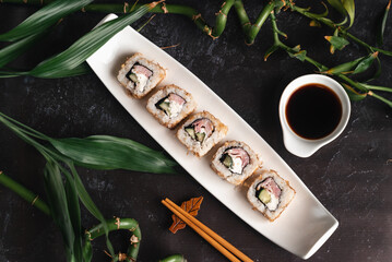 Fresh sushi on white plate. Japanese traditional food. Chopsticks, soy sauce, bamboo branches on black background. Asian style