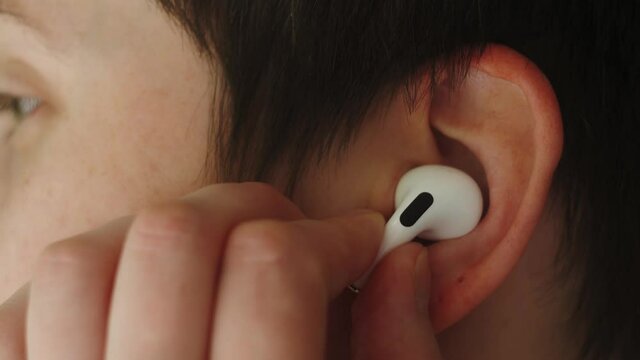 Portrait of a beautiful young, with headphones wireless in her ear, listens to music close up macro super. Student happy with earpods handsfree bluetooth, girl smiling, looking down.