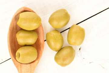 Tinned green pitted olives, close-up, on a wooden table.