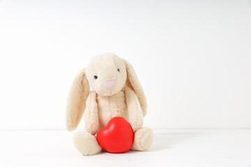 Brown rabbit doll sitting with red heart on white background.