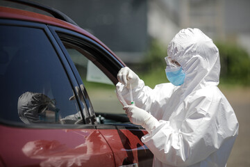 A health worker uses a CPR test (mouth and nasal swab) on a person inside a car to determine the...