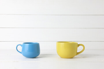 Blue cup and yellow cup coffee on white wood background with copy space.
