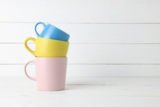 Stacked Blue, Pink And Yellow Coffee Mugs On White Wood Background.