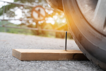 Close up a metal nail on board wood nearly to puncture into wheel tire