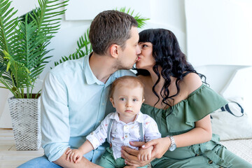 Obraz premium mom and dad kissing, baby in arms looking at the camera, happy family concept, family Day