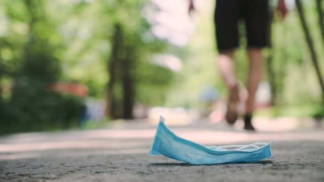 A passing man accidentally drops or intentionally throws out a medical mask. The surgical mask falls to the ground. Slow motion.