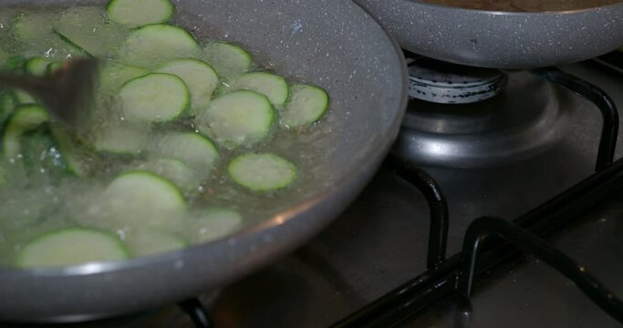 Dinner time at home with the family. Sliced zucchini fry in oil in a pan in the kitchen.