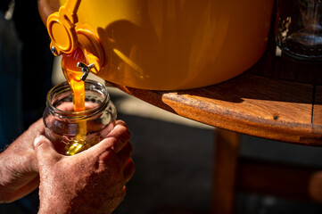 Bottling of flows honey. Beekeeper holds in his hand jar into which honey flows from a barrel.