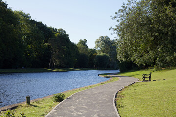 Path meandering along beside still lake with bench on grass
