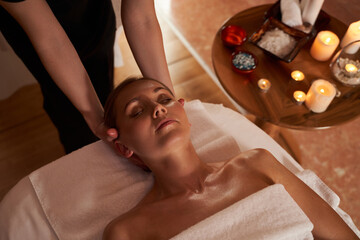 Hands of massage therapist under the head of young woman