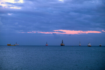 Ships anchored in the outer harbor. Darkening sky with dramatic clouds, dark blue sea surface, pink...