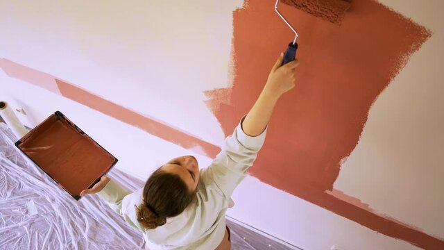 brunette colours white wall into brown holding roller set in hands standing on floor during apartment renovation at self isolation in new flat vertical view