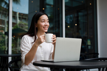 Asian woman working with computer laptop and drinking coffee in coffee shop cafe smile and happy face