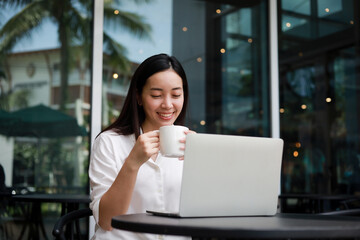 Asian woman working with computer laptop and drinking coffee in coffee shop cafe smile and happy face