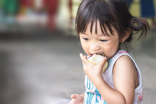 Selective​ focus.​ Portrait​ image​ of​ 2-3​ years​ old​ of​ baby.​ Happy​ Asian​ child​ girl​ eating​ some​ sweet​ donut or​ chocolate​ bread.​ Kid​ and​ food​ concept.