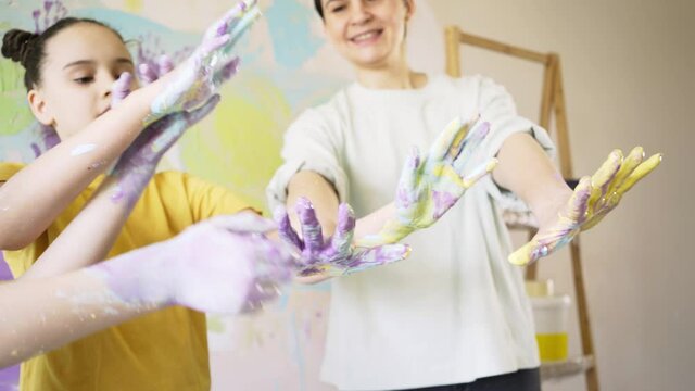 funny children with mother in white t-shirt show hands with various paints against coloured wall in new apartment before son birthday close view