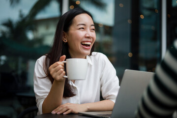 Asian woman working with computer laptop and drinking coffee in coffee shop cafe smile and happy face and talking with friend - 364124813