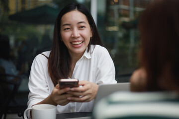 Asian woman working with computer laptop and drinking coffee in coffee shop cafe smile and happy face and talking with friend