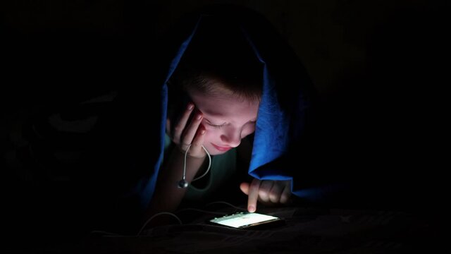 young children using cell phone hidden under bed covers. The child listens to music and looks at the photos