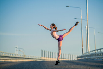 Girl gymnast engaged in the summer on the street, on a background of blue sky, twine, stretching, arabesque