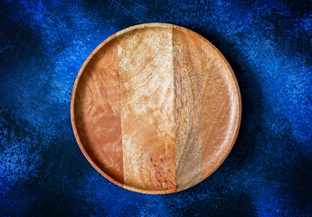 Top view of wooden round plate for pizza on contrast dark blue background. Mockup for food, a combination of beautiful textures of a wooden tray and a background. Horizontal orientation, copy space
