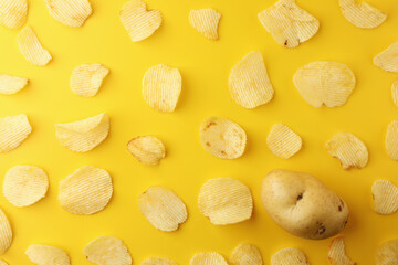 Crispy potato chips snacks with one potato on a yellow background. Image top view, flat lay.