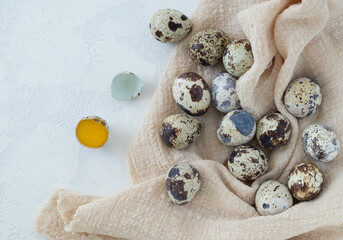 Many fresh quail eggs lie on a light linen napkinon a light surface with plaster texture. Close-up, horizontal orientation, top view. Copy space. Selective focus. Healthy food is a concept.