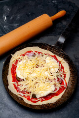 Fresh raw Pizza in an rustic iron Pan on a Slate Plate, the rolling pin is lying beside and the slate is covered with flour.
