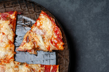 Slice of a fresh Pizza in an rustic iron Pan on a Slate Plate. Close up.