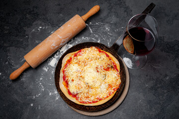 Fresh Pizza in an rustic iron Pan on a Slate Plate with a Glass of red Wine. A rolling pin lying beside and the slate is covered with flour.